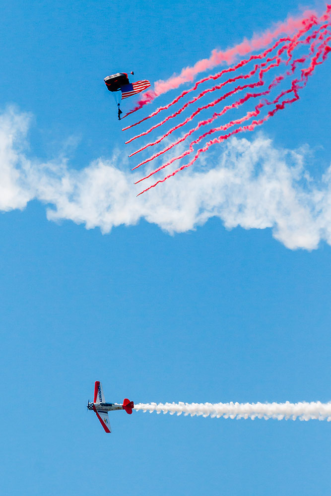 Photo by Rick Pepper - 2012 Mankato Air Show - The parachute jumper and a Shell Aerobatic aircraft perform the opening ceremony displaying the American flag