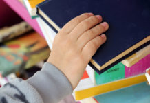 Kid's Hand Taking Book from a Shelf in Public Library.