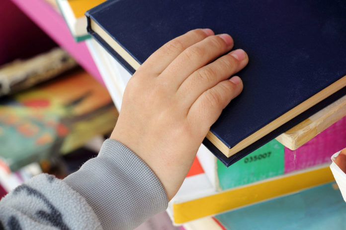 Kid's Hand Taking Book from a Shelf in Public Library.