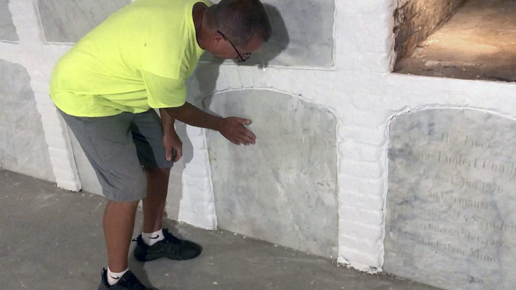 Photo by Mike Lagerquist - Caretaker Terry Miller shows the face of one of the basement crypts that originally held the bodies of priests.