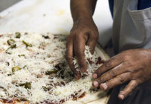 Photo by Casey Ek - Hensta piles topppings onto a pizza destined for a pickup order. While he learned the skills of making food over 25 years from mentors, colleagues and through passive observation, Hensta believes customer feedback has been equally important in refining his dishes. He has used that feedback to determine the amount of toppings typical customers want.