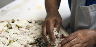 Photo by Casey Ek - Hensta piles topppings onto a pizza destined for a pickup order. While he learned the skills of making food over 25 years from mentors, colleagues and through passive observation, Hensta believes customer feedback has been equally important in refining his dishes. He has used that feedback to determine the amount of toppings typical customers want.