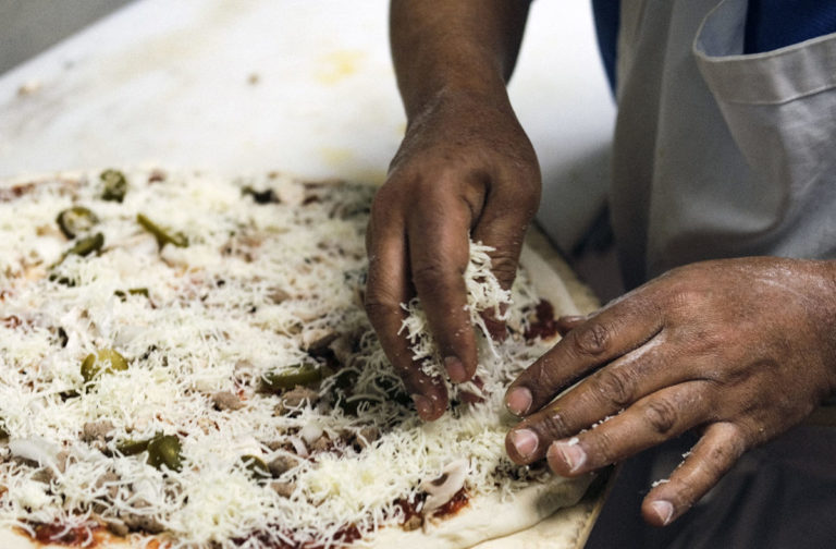 Photo by Casey Ek - Hensta piles topppings onto a pizza destined for a pickup order. While he learned the skills of making food over 25 years from mentors, colleagues and through passive observation, Hensta believes customer feedback has been equally important in refining his dishes. He has used that feedback to determine the amount of toppings typical customers want.