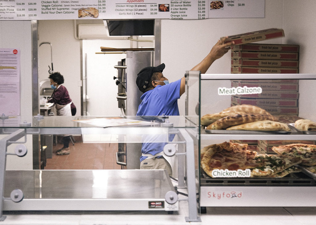 Photo by Casey Ek - Hensta, right, stacks folded pizza boxes while his sister Akberet works in the kitchen of Great New York Pizza. The restaurant has embraced a modified approach to doing business in the wake of the COVID-19 pandemic and, like most restaurants, has had to adapt to selling takeout food like never before.