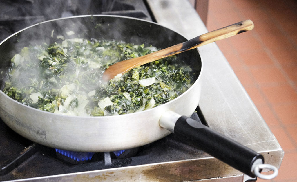 Photo by Casey Ek - A pan of a spinach filling simmers on a stovetop. After joining the restaurant industry 25 years ago after leaving his home country of Eritrea, Hensta has embraced life in America through his cooking.