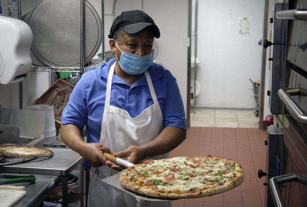Photo by Casey Ek - Hensta pulls a pizza from an oven at Great New York Pizza.