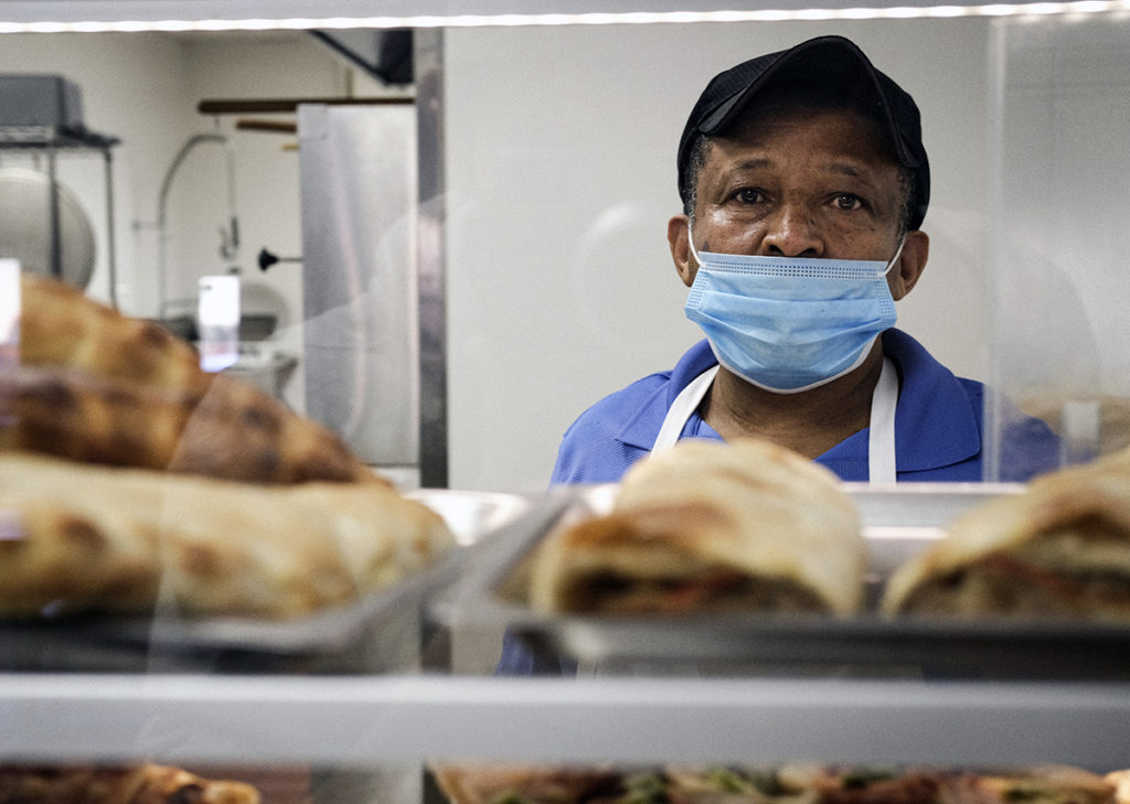 Photo by Casey Ek - Shot through a display case showcasing various a la carte items like calzones and pizza by the slice, Hensta stops to have his portrait taken.