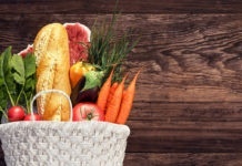 White basket full of groceries and vegetables on wood background