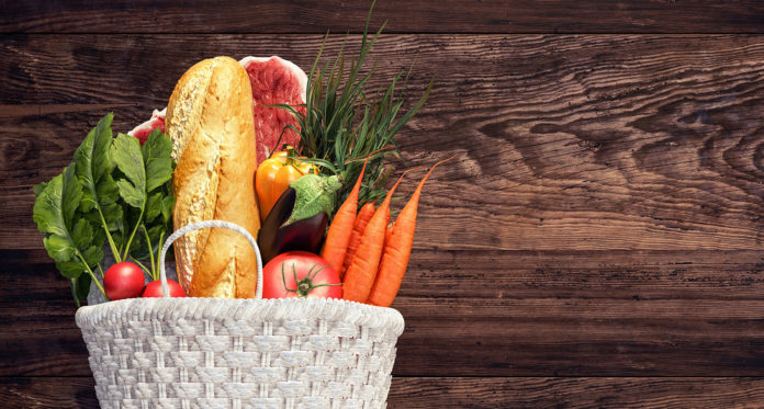 White basket full of groceries and vegetables on wood background