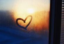 Heart drawn on a misty window and sunset on the background