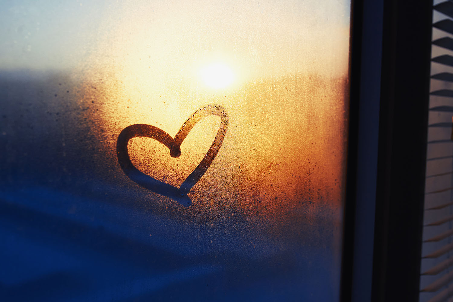 Heart drawn on a misty window and sunset on the background